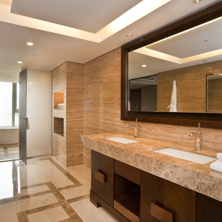 Lifestyle image of a Hotel style bathroom, with marble floor tiles, dark brown wooden cabinet and marble countertop, inset basins with chrome taps and a wooden backed rectangular mirror