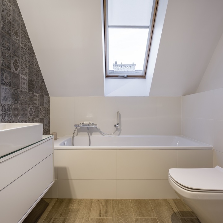 Lifestyle image a small attic bathroom, with a built in bath, wall hung washbasin unit, back to wall toilet and skylight