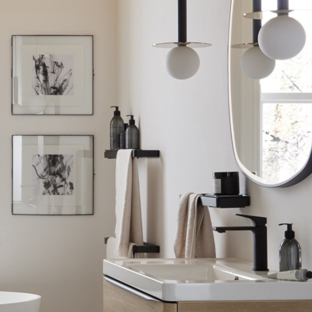 Product lifestyle image of vado cameo muse 150mm matt black glass shelf insert and wall mounted frame with towel hanging beside underneath large mirror with beauty product. MUS-085-15-BLK and MUS-184-45-MB