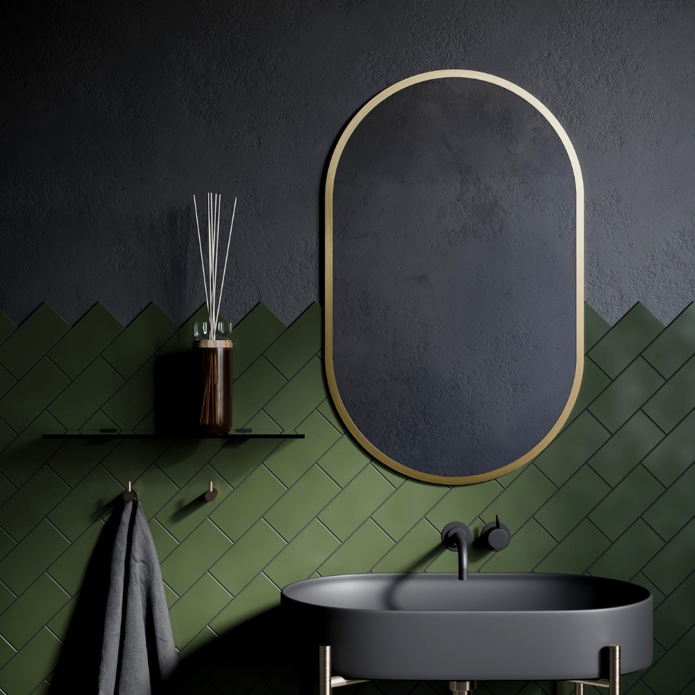 Lifestyle image of the Origins Living Docklands 500mm x 800mm Brushed Brass Capsule Mirror mounted on black and green wall, in-front of a modern, grey coloured basin. DKL-00C058-BB