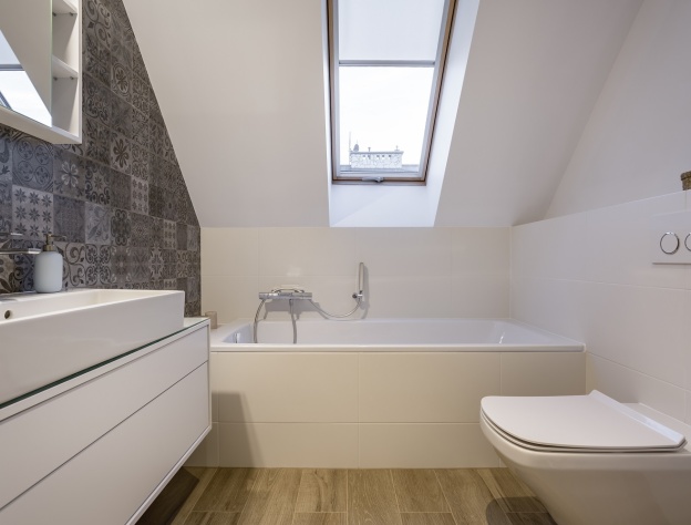 Lifestyle image a small attic bathroom, with a built in bath, wall hung washbasin unit, back to wall toilet and skylight